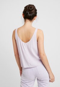 Lavender sleeveless top with a V-back, featuring a loose fit and soft texture. Worn with matching pastel pants, emphasizing simplicity.