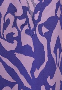 Indumento viola con un audace motivo astratto in tonalità di lavanda più chiare, caratterizzato da un design a V e una texture morbida.