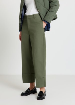 Pantalon large couleur vert olive en tissu texturé, doté d'une ceinture classique et de revers ourlés, associé à des mocassins noirs.