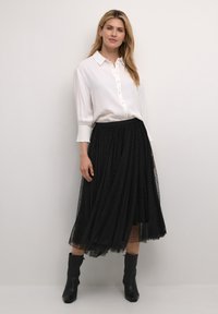 White button-up shirt with cuffed sleeves, paired with a pleated black tulle skirt featuring polka dots. Black ankle boots complete the outfit.