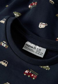 Marinblå bomulls-T-shirt med ett mönster av färgstarka fordon, inklusive en brandbil, bilar och ambulanser. Ribbad rund halsringning.