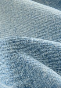 Ljusblå denimtyg med en texturerad yta, som visar subtila variationer i färg och väv mönster, draperad i mjuka veck.