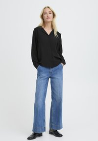 Schwarzes Langarmhemd mit Kragen, kombiniert mit weit geschnittenen blauen Jeans und schwarzen Knöchelschuhen. Das Hemd hat eine entspannte Passform.