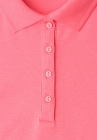 Polo rose devant montrant le col replié et quatre boutons alignés verticalement sur la patte de boutonnage.