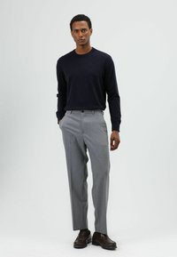 Marineblauwe trui met ronde hals gecombineerd met lichtgrijze, op maat gemaakte broek. Schoenen zijn donkerbruin leer. Eenvoudig ontwerp met fijne breistructuur.