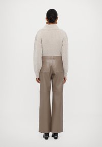 Beige ribbestrikket genser med vide ermer, sammen med høyt liv, lysebrune vide bukser. Svarte sko med dekorative detaljer.