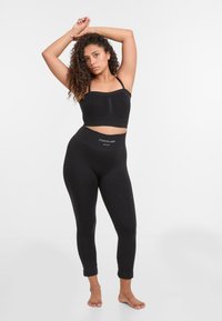 Zwarte cropped top met dunne banden en zwarte high-waisted leggings met een logo op de tailleband. Gladde textuur, aangesloten ontwerp.