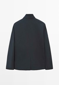 Sort jakke med høj krave, designet med lige linjer og en slids bagpå for nem bevægelse. Glat, mat stoftekstur.