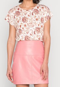 Blusa de manga corta en color crema con un patrón floral rojo, combinada con una minifalda de cuero rosa ajustada. Telas texturizadas y detalles de diseño distintivos.