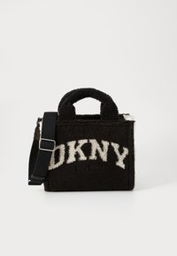 Sac fourre-tout en fausse laine de mouton noir de DKNY avec logo blanc, poignées supérieures et bandoulière ajustable noire sur fond blanc.