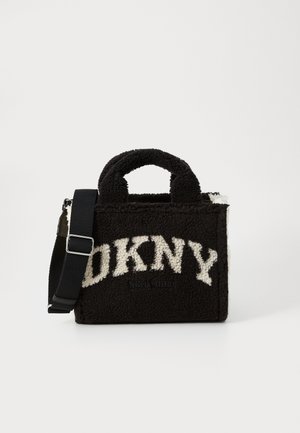 Zwarte nepbont DKNY draagtas met wit logo, bovenhandvaten en verstelbare zwarte schouderriem op een witte achtergrond.