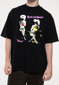 Black oversized t-shirt featuring colorful graphic print of two figures in vibrant attire. Text reads "Siouxsie and the Banshees."