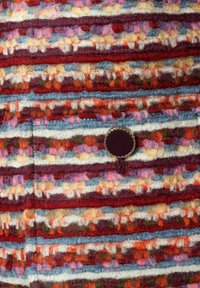 Wollen stof in horizontale strepen van rood, blauw, roze, crème en groen. Bevat een ronde, donkerbruine knop met een gevlochten rand.