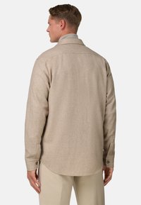 Beige košile s límečkem, texturovaná tkanina, dlouhé rukávy, zapínací manžety a zaoblený lem, předvedená z pohledu zezadu.