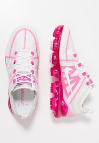 Scarpe da ginnastica bianche con accenti rosa, in tessuto a rete, superficie testurizzata e suole trasparenti rosa, dotate di un logo bianco prominente e lacci.