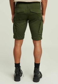 Pantaloni cargo verde oliva con più tasche, risvolti e materiale in misto cotone. Stivali da combattimento neri con superficie testurizzata.