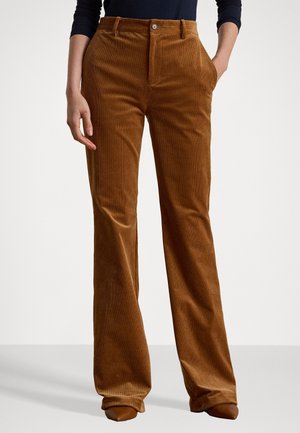 Brown corduroy wide-leg pants worn by person with one hand in pocket, paired with dark long-sleeve top and brown pointed shoes.
