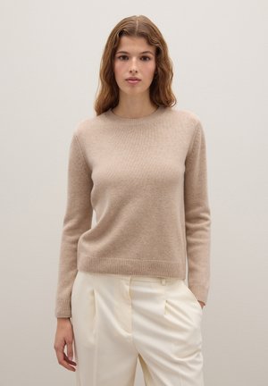 Beige Strickpullover mit langen Ärmeln, rundem Halsausschnitt und geripptem Saum. Kombiniert mit cremefarbigen, hochtaillierten Hosen. Glatte Textur.