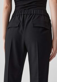 Pantaloni neri con una finitura testurizzata, dotati di un elastico in vita, pince laterali e due tasche posteriori piatte. Adatti per un look informale.
