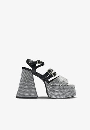 Sandale cu platformă neagră și argintie, cu trei barete cu cataramă cu strasuri și toc bloc larg, texturat.