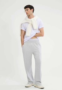 Jasnoszare bawełniane joggersy z elastycznym paskiem w talii i bocznymi kieszeniami, w połączeniu z białą koszulką z okrągłym dekoltem i kremowym swetrem zarzuconym na ramionach.