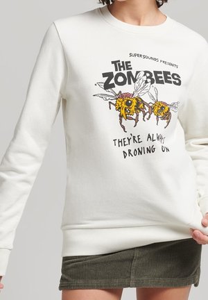 Sweat-shirt blanc avec des abeilles zombifiées en dessin animé et texte "The Zombees, They're Always Droning On,", porté avec une jupe vert olive.