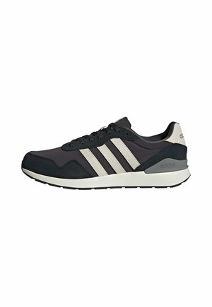 Zapatilla Adidas negra y gris con rayas blancas, cierre de cordones en la parte delantera y suela acolchada, mostrada de perfil sobre un fondo blanco.