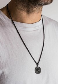 Sort kæde-nederdel med en rund vedhæng med løve-design, sat mod en simpel hvid t-shirt.