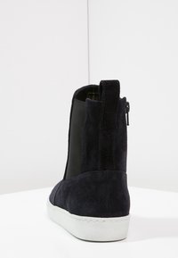 Bottine en daim marine avec panneaux latéraux élastiques, un dos texturé et une semelle en caoutchouc blanc. Équipée d'une fermeture à glissière sur le côté et de détails de couture minimalistes.