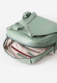Zaino in pelle verde chiaro con apertura con zip, fodera beige testurizzata e accenti rossi all'interno. Include numerosi scomparti e tasche.