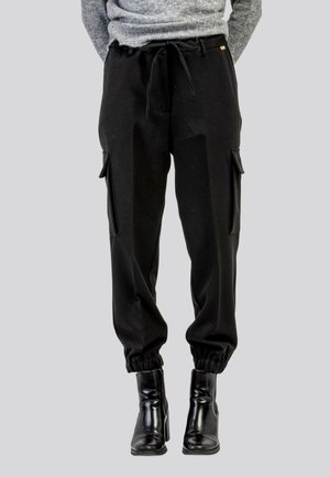 Pantaloni cargo neri con vita regolabile tramite cordino, polsini elasticizzati e tasche laterali. Realizzati in tessuto morbido con una vestibilità comoda, abbinati a stivali alla caviglia.