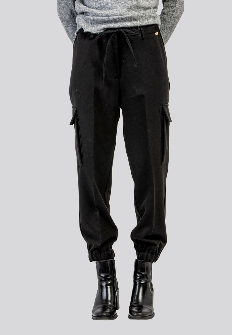 Pantaloni cargo neri con vita regolabile tramite cordino, polsini elasticizzati e tasche laterali. Realizzati in tessuto morbido con una vestibilità comoda, abbinati a stivali alla caviglia.