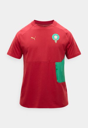 Tricou sport roșu cu mâneci scurte și buzunar lateral verde, logo aurit Puma pe pieptul drept și emblema echipei naționale de fotbal a Marocului pe pieptul stâng.