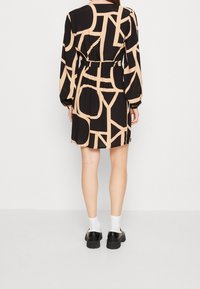 Kurzes schwarzes Kleid mit einem beigen abstrakten Muster, langen Ärmeln, elastischem Bund und lockerer Passform, kombiniert mit schwarzen Schuhen und weißen Socken.