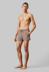 Costume da bagno marroni realizzati in un tessuto leggero, dotati di una cintura elastica con cordino e tasche laterali per riporre gli oggetti.