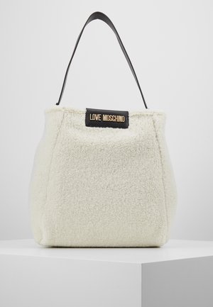 Biała torebka z ekologicznego baranka z czarnym skórzanym uchwytem i złotą tabliczką z logo "LOVE MOSCHINO" z przodu, prezentowana na białym pedestale.