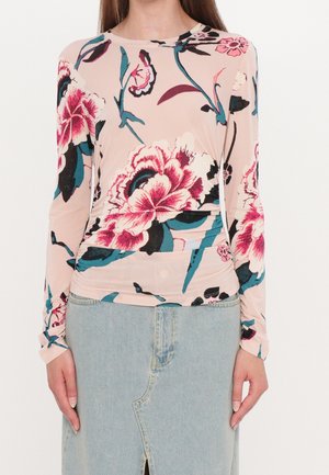 Vrouw draagt een beige longsleeve met grote roze bloemenprint en een lichtblauwe denim rok met voorsplit.