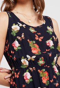 Květinové šaty bez rukávů s tmavě námořnickým pozadím, zdobené růžemi a motýly; elastický pas, jemný materiál a kulatý výstřih.