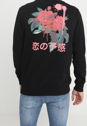 Sudadera negra con un gráfico floral en rojo y verde en la parte posterior, con salpicaduras de pintura y texto japonés debajo del diseño.