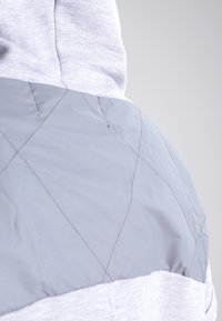 Gray quilted back panel with diagonal stitching, paired with a light gray fabric hood and body. Smooth texture, casual design.