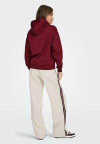 Felpa bordeaux con una vestibilità comoda, polsini e orlo a costine. Abbinata a pantaloni beige chiaro con strisce maroon lungo i lati.