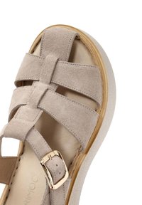 Sandal in suede beige con cinturini incrociati e fibbia dorata, caratterizzata da una suola a piattaforma leggera con una finitura texture e un accento in legno naturale.