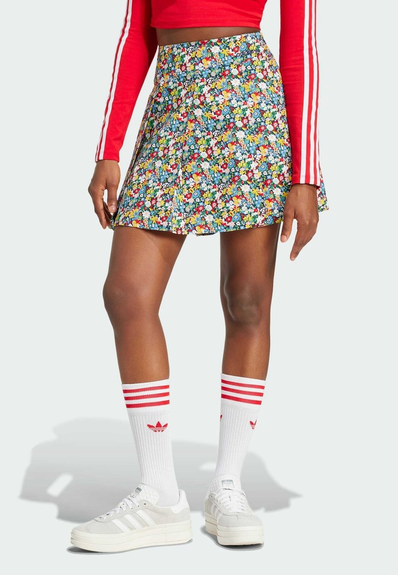 Falda floral de tela multicolor, diseño plisado, de longitud por encima de la rodilla. Combinada con calcetas a rayas rojas y blancas y zapatillas blancas.