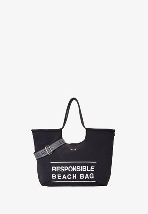 Zwarte stoffen strandtas met dubbele handvatten, verstelbare grijze schouderband en witte tekst "VERANTWOORDE STRANDTAS." Eenvoudig, ruim ontwerp.