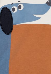 Bomullsstoff med et design av en tegneseriehund med blått hode, brunt kropp og svart øre, pyntet med søm detaljer og store øyne.
