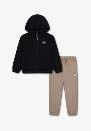 Veste à capuche noire zippée avec poches avant et pantalon beige à taille élastique, tous deux arborant de petits logos Converse All Star.