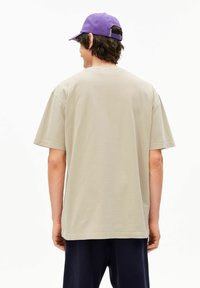 Beige katoenen t-shirt met korte mouwen, een losse pasvorm en een rechte zoom. Paarse pet die achterstevoren wordt gedragen, voegt contrast toe aan de outfit.