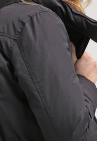 Black puffer jacket with quilted texture, featuring a high collar and snug fit, showcasing a smooth, matte finish.