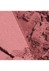 Poudre de maquillage rose pressée, partiellement écrasée, montrant une surface texturée et des morceaux cassés en vue rapprochée.