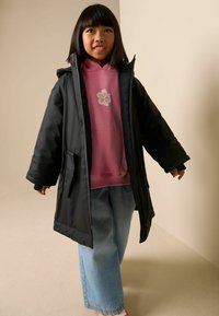 Juodas pūkinis paltas su gaubtu ant rožinės gaubtuotos su gėlių raštu, derinamas su plačiomis mėlynomis džinsais. Kasdienis žiemos aprangos komplektas.